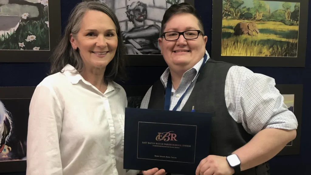Megan Hall, East Baton Rouge Parish District Teacher of the Year, smiling with a colleague while holding her teaching award certificate