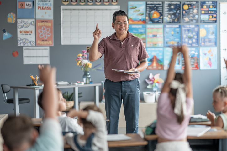 Classroom setting with a teacher leading an educational session with attentive students raising hands, showing engagement and learning.