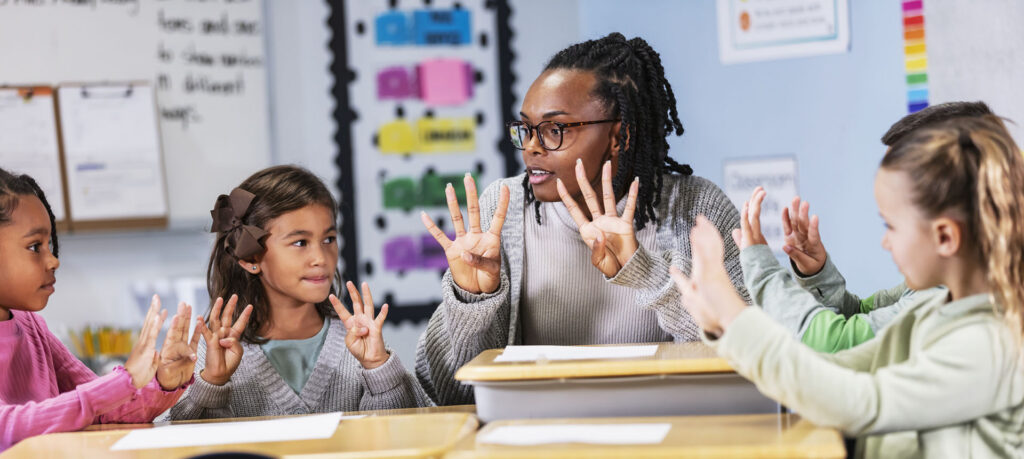 An elementary teacher with four children in the classroom. The students, three girls and a boy, are sitting at desks having a lesson.